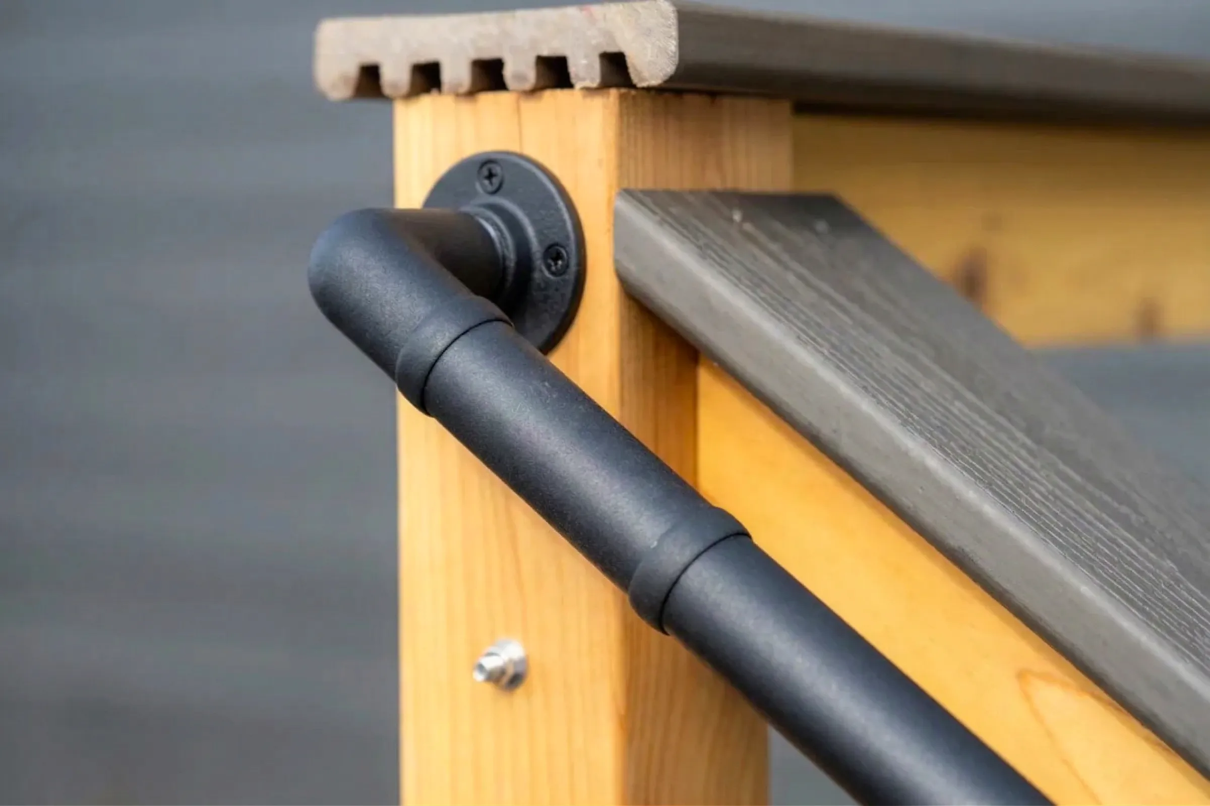 Close-up of a custom deck railing: matte black metal handrail on a natural wood post with grey composite top rail
